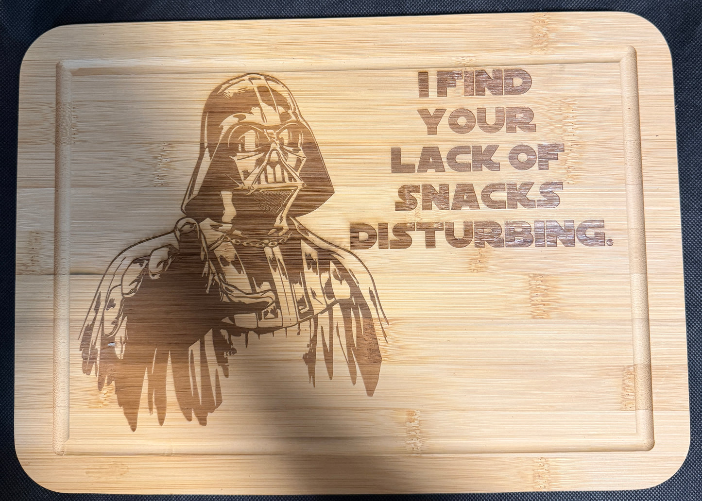 Wooden cutting board with Darth Vader engraving and text on a dark background