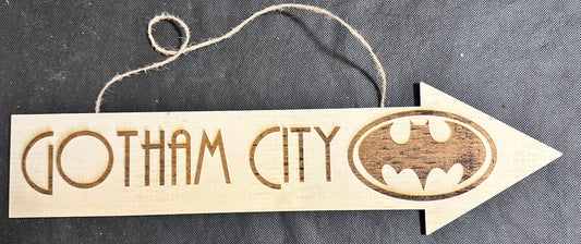 Wooden arrow-shaped sign with 'Gotham City' and Batman logo on a dark background