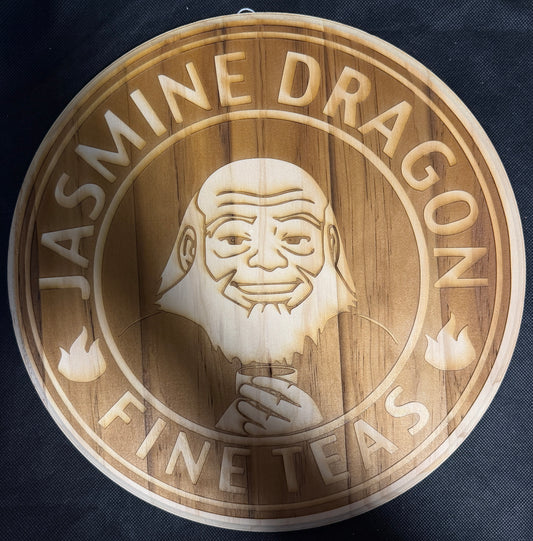 Wooden sign with engraved face and 'Jasmine Dragon Fine Teas' text on a dark background
