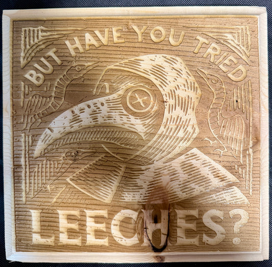 Wooden block with engraved plague doctor and text 'But have you tried leeches?'